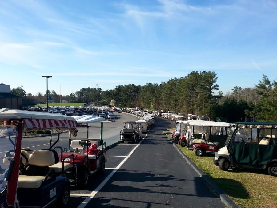 All but three parking spaces in the golf cart parking lot appear to be full and overflowing on the grass.