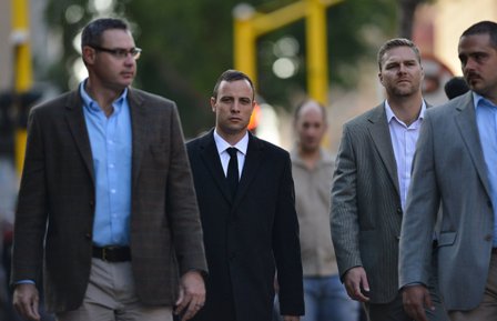 South African paralympic athlete Oscar Pistorius, center, is escorted as he walks to the high court in Pretoria, South Africa, Monday, April 7, 2014. Pistorius stands trial for the premeditated murder of his model girlfriend Reeva Steenkamp at his home in Pretoria East. 