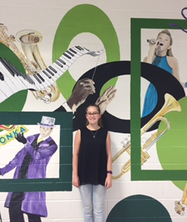 Another talent show participant, freshman Ann-Charlotte Langet, smiles broadly by the mural outside the auditorium.