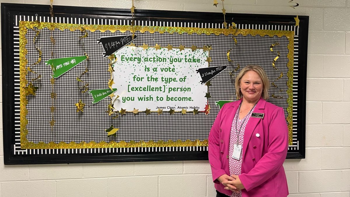 Amy Hammock poses in front of a billboard in the hallway that exemplifies her goal for the year- "making excellence a habit."