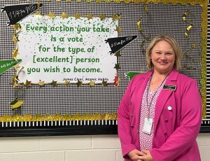 Amy Hammock poses in front of a billboard in the hallway that exemplifies her goal for the year- "making excellence a habit."