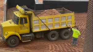Construction worker guiding a loaded dump truck through the construction site.