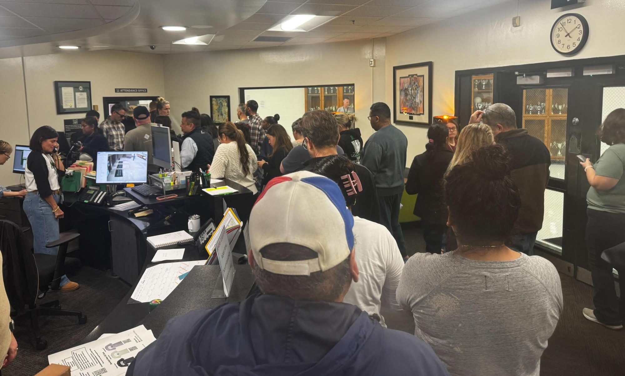 Parents waiting in the front office to pick their kids up while a line of students form to check out.