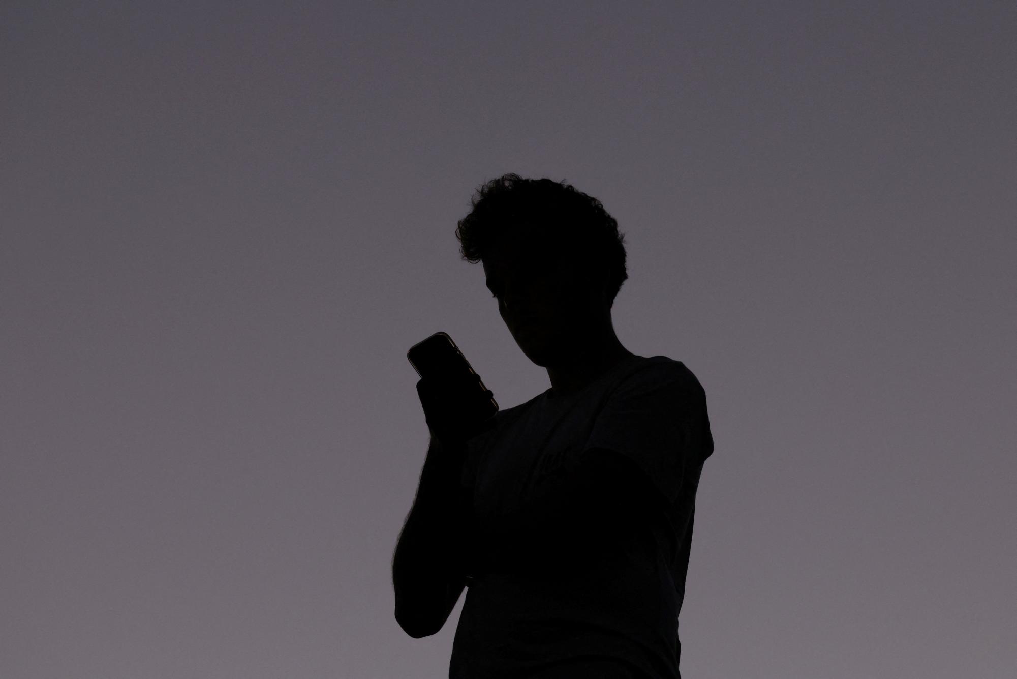 A man uses a mobile phone, ahead of new law banning social media for users under 16 in Australia, at dusk in Brisbane, Australia, December 8, 2025. REUTERS/Hollie Adams